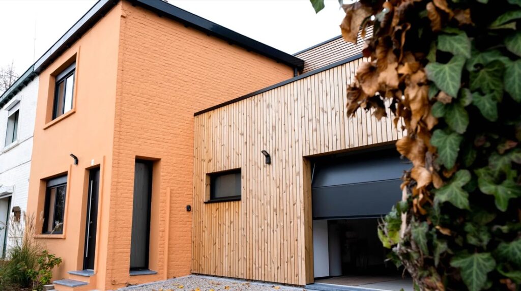 Garage en ossature bois accolé à une maison de brique peinte, bardage vertical clair et porte sectionnelle anthracite