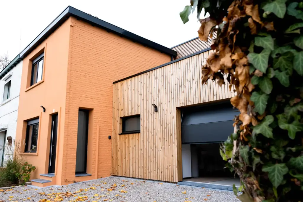 Garage en ossature bois vu de biais, bardage vertical à claire-voie et porte entrouverte