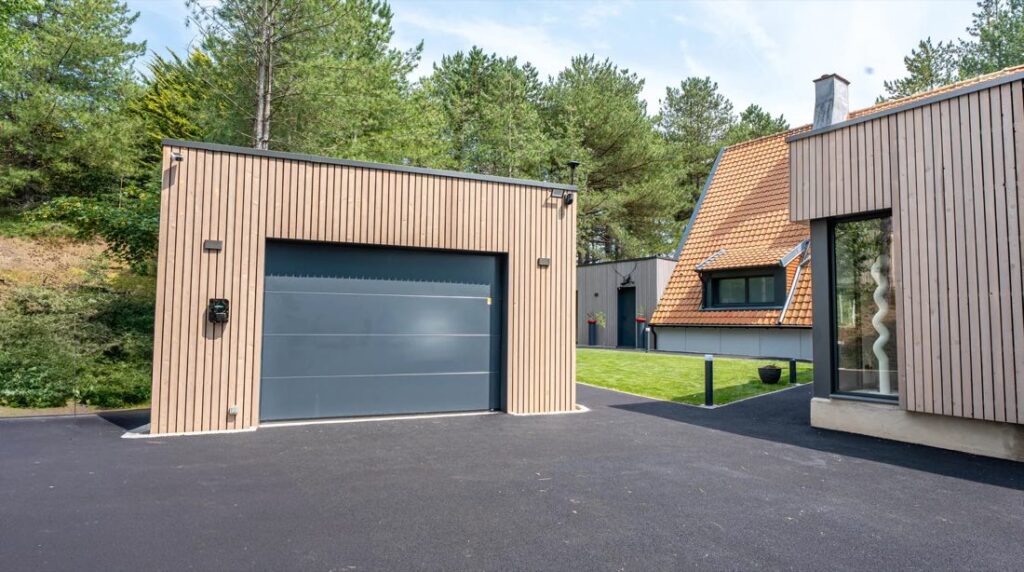 Garage indépendant en ossature bois, bardage vertical clair, toit plat et porte sectionnelle grise