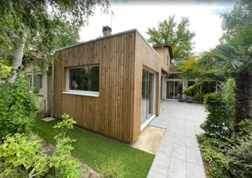 Mon Extension Bois Bordeaux 12 Extension en bois à bardage vertical et grande baie, vue du jardin avec palmier et allée dallée