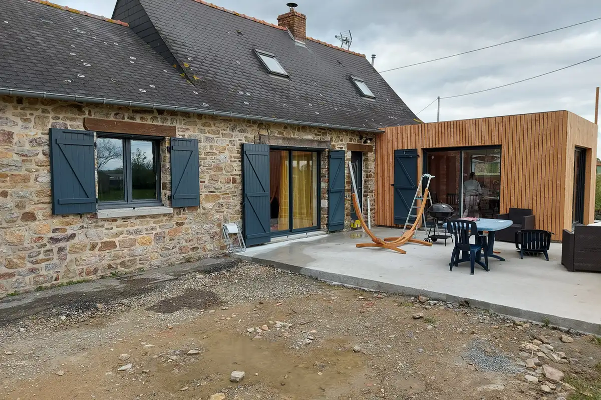 Mon Extension Bois Rennes 8 Longère en pierre et sa double extension en kit, bardage bois vertical, volets bleus et terrasse, en Ille-et-Vilaine