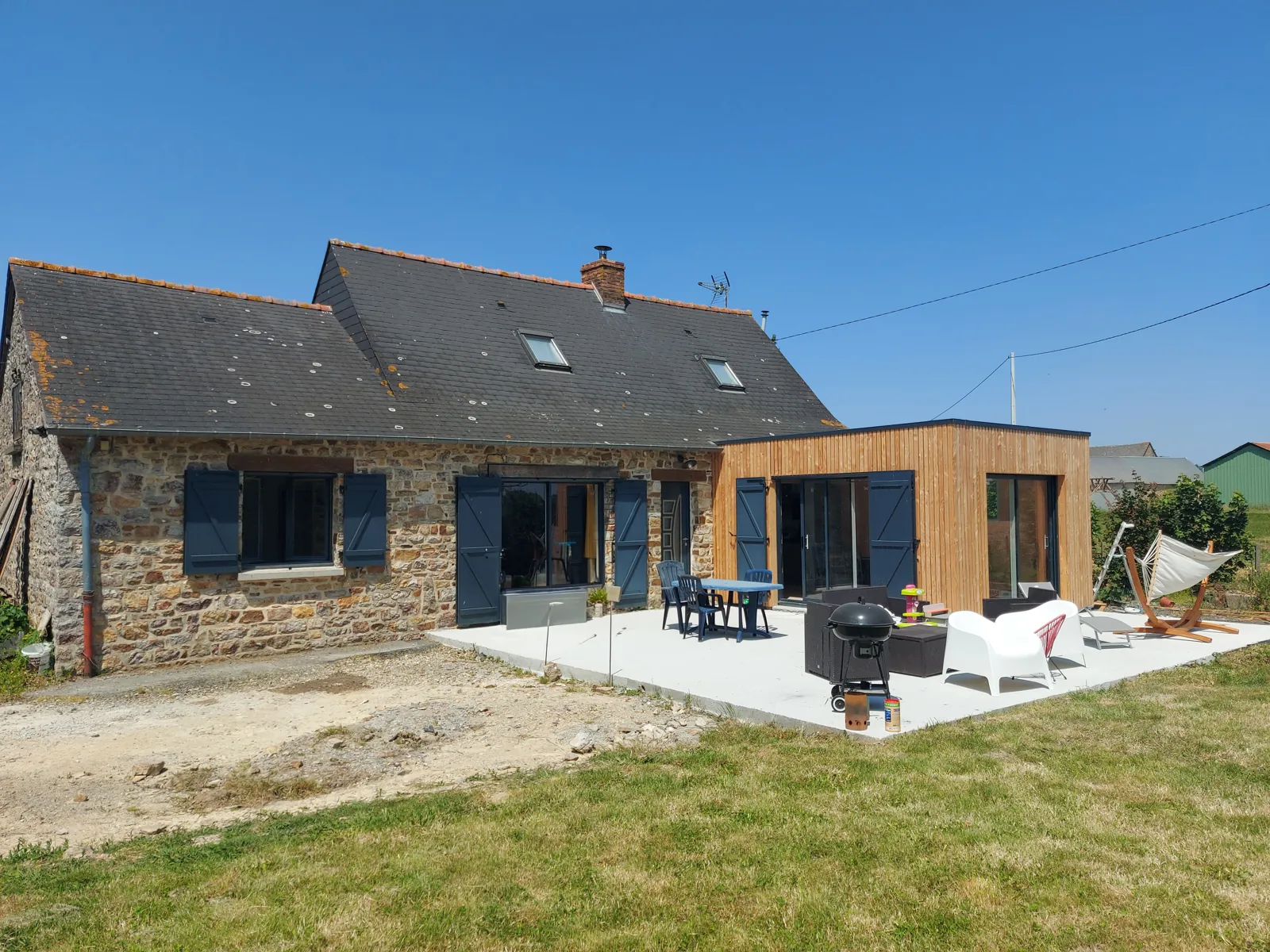 Fondations d'une extension bois : dalle, plots ou pieux vissés ? 14 Extension en ossature bois à bardage clair contre une maison de campagne en pierre et toit d'ardoise