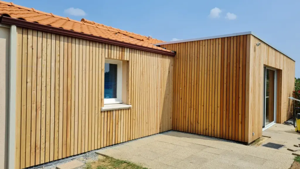 Angle d une extension en bardage mélèze vertical contre un pavillon à toiture en tuiles rouges