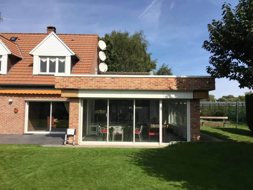Extension à toit plat et grande baie vitrée contre un pavillon en brique et tuiles